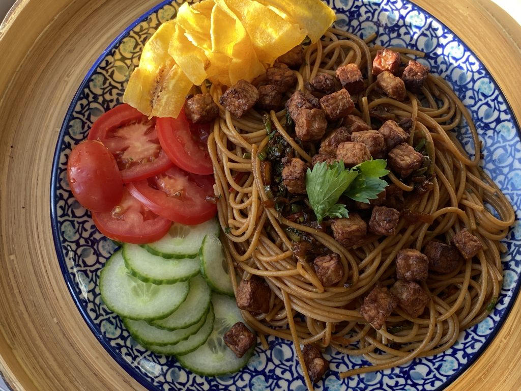 Een bord met Surinaamse bami, komkommer, tomaat en bananenchips
