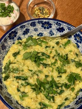 Een schaal met khichdi met spinazie en specerijen, een bakje ui-tomaatraita en een bakje met mukhwas