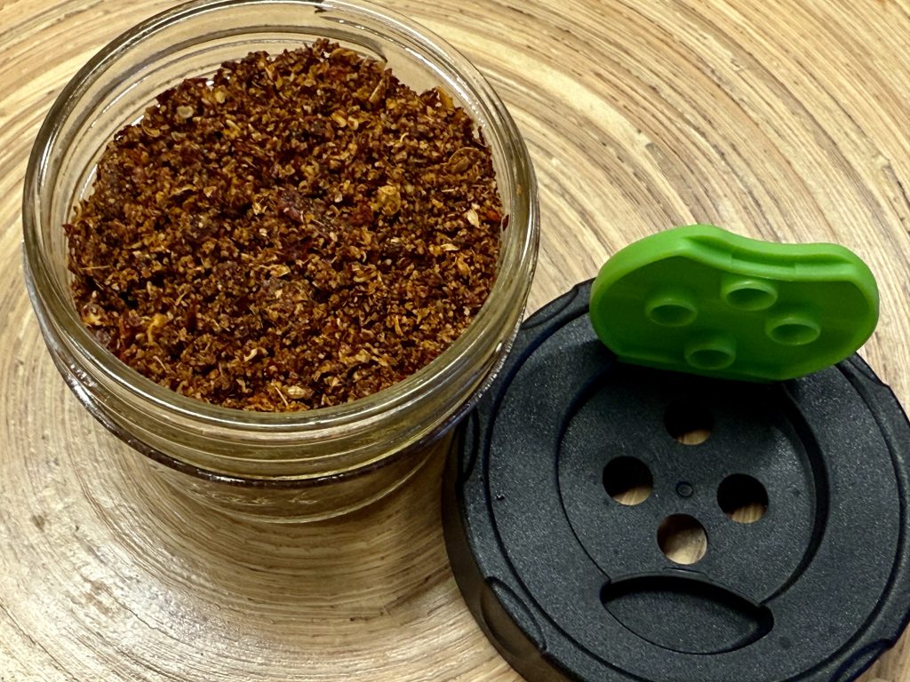 Glazen potje met daarnaast een deksel met gaatjes, erin sambar kruiden