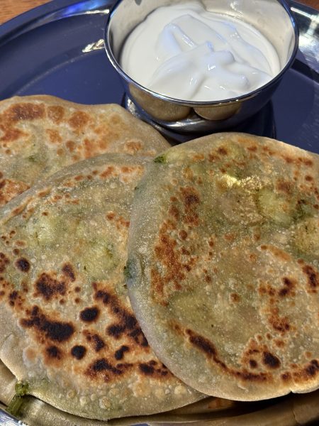 Aan roestvrij stalen bord met daarop een bakje met raita en drie aloo paratha’s