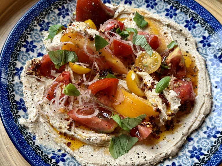 Een Bunzlau bord met daarop een bedje van ricotta spread, daarop heirloomtomaten besprenkeld met balsamico-azijn en chili olie
