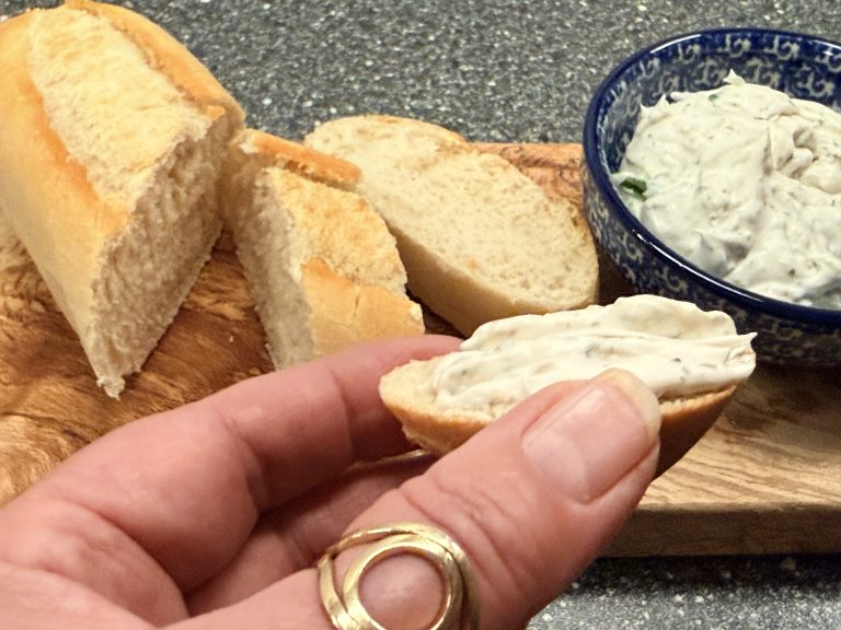 Mijn hand die een stukje stokbrood vasthoudt met daarop de smakelijke Philadelpia spread